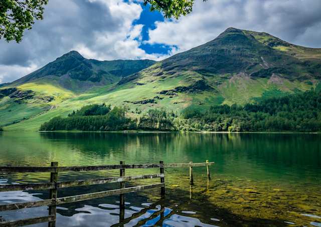 A tall green hill behind a serene lake in the Lake District, England, UK