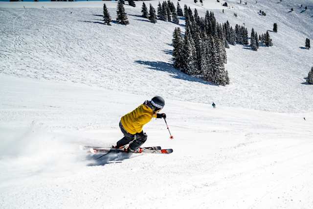 Person skiing down a snowy mountain in front of trees in Vail, Colorado, US