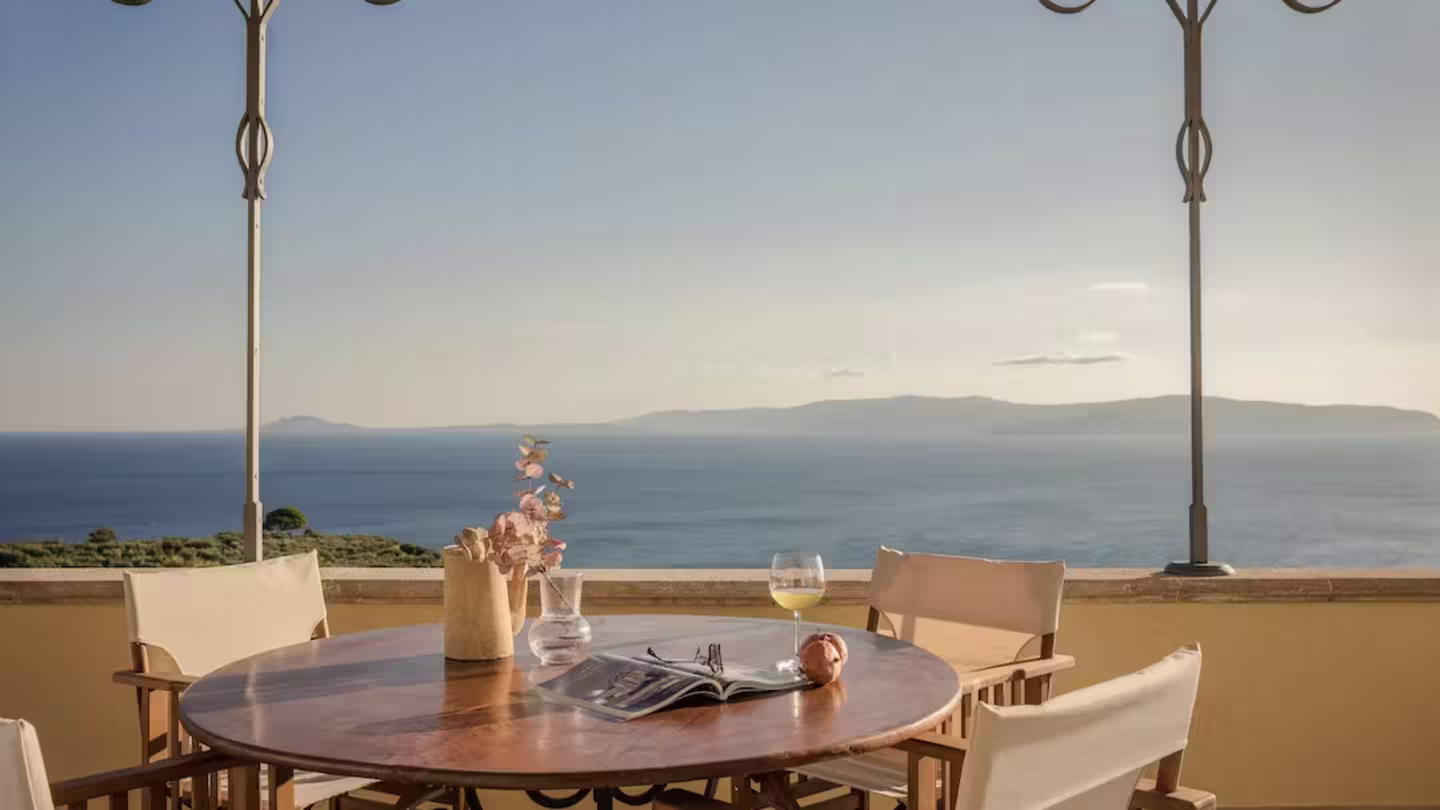 A table on a terrace with a glass of wine and magazine facing the sea, Plum Guide home 'Sunset Haze' in Kefalonia, Greece