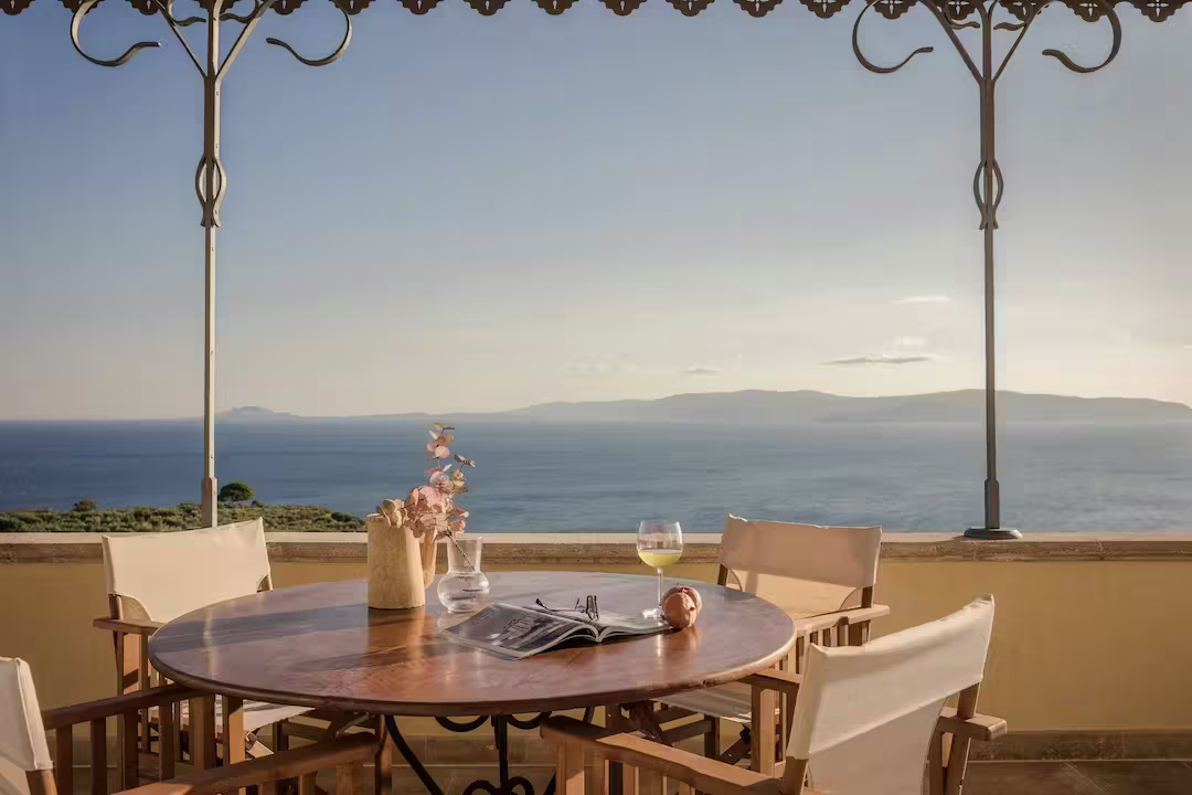 A table on a terrace with a glass of wine and magazine facing the sea, Plum Guide home 'Sunset Haze' in Kefalonia, Greece