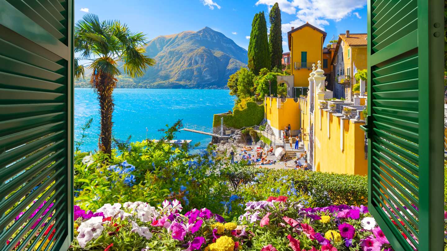 View through an open window with shutters of the lake, mountains and the picturesque village of Varenna, Lake Como