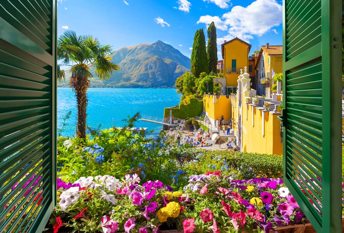 View through an open window with shutters of the lake, mountains and the picturesque village of Varenna, Lake Como