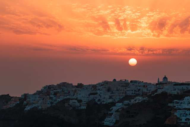 An orange sun and orange sky over houses in Oia, Santorini, Greece at sunset