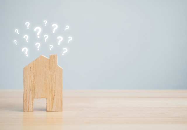 A small wooden model house on a table surrounded by question marks