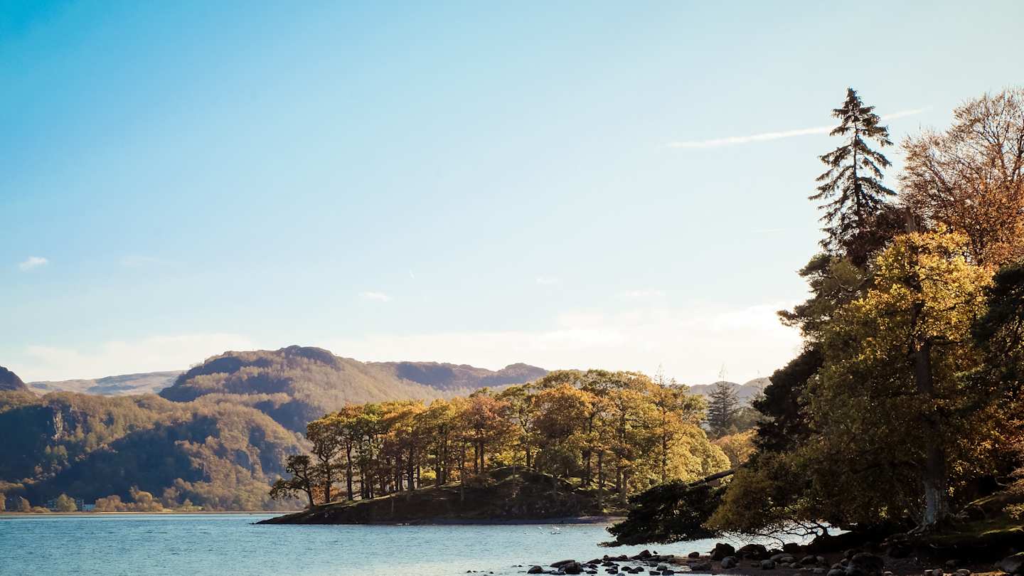 A still lake amongst tall trees and hills on a sunny day, Lake District, Keswick, Cumbria, UK