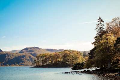 A still lake amongst tall trees and hills on a sunny day, Lake District, Keswick, Cumbria, UK