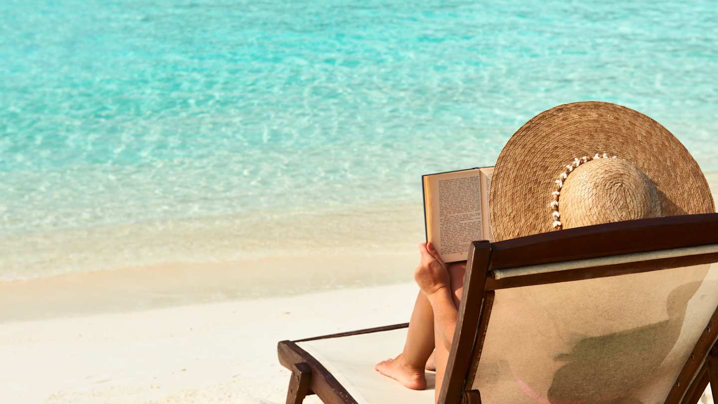 A woman sunbathing at the beach reading a book