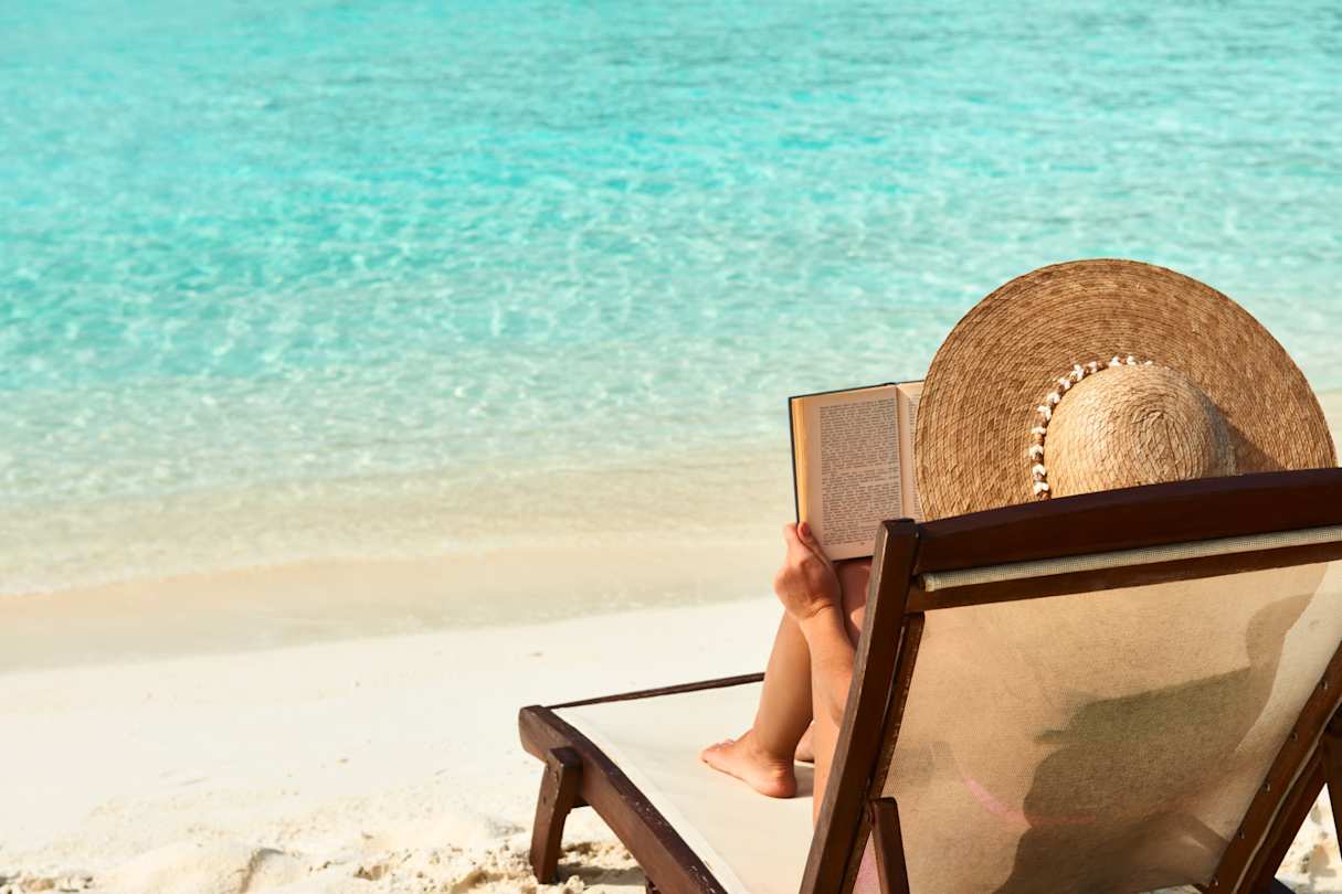 A woman sunbathing at the beach reading a book