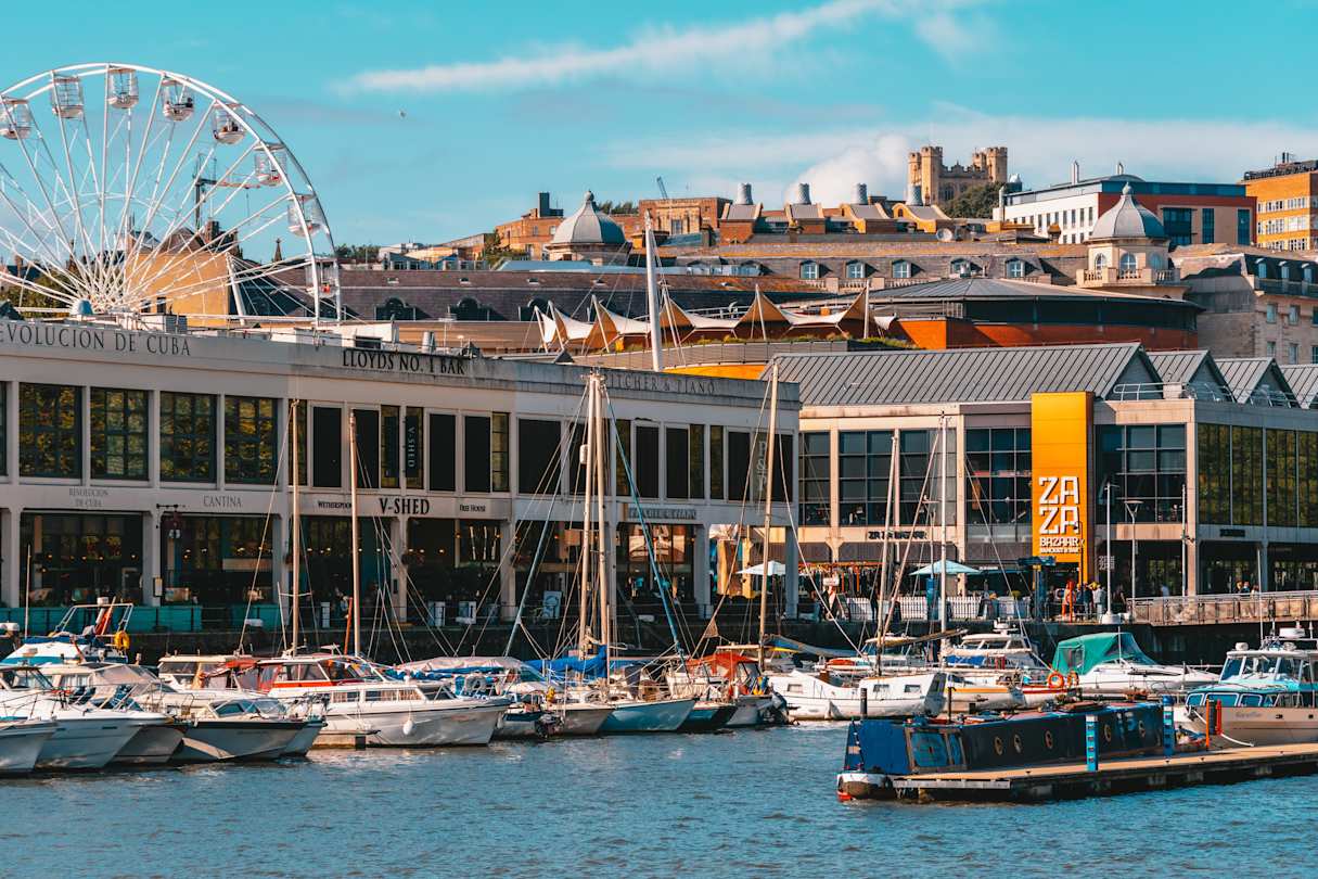 Boats in the water by buildings and a ferris wheel at Bristol Harbourside, England, UK