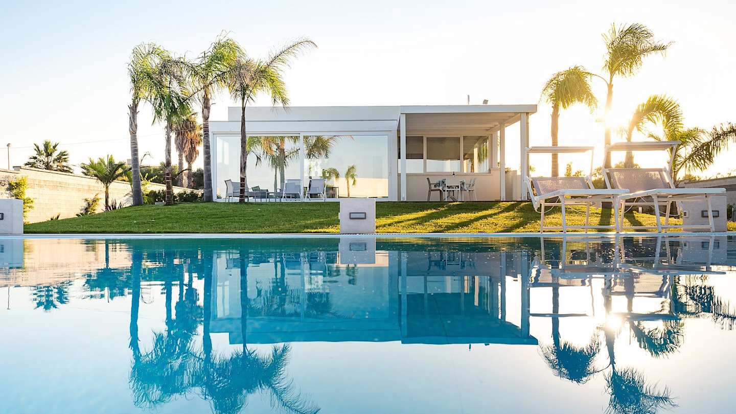 Plum Guide home Sicilian Cubism, with palm trees reflected in the swimming pool at sunset, Sicily, Italy