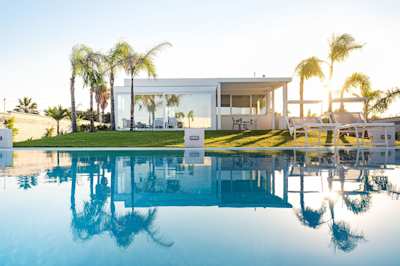 Plum Guide home Sicilian Cubism, with palm trees reflected in the swimming pool at sunset, Sicily, Italy