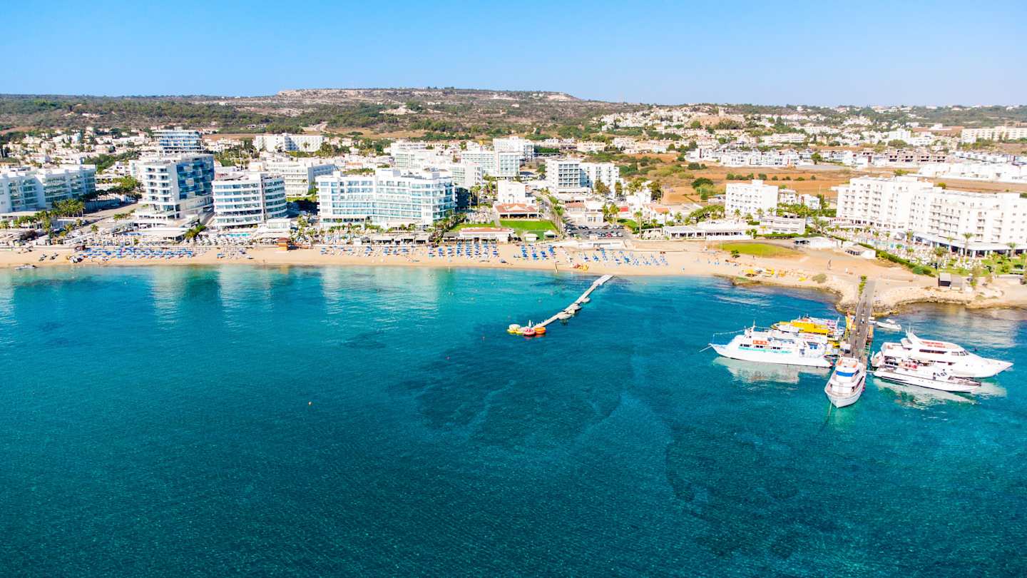 Ariel view of Sunrise Beach's golden sand, blue sea and waterfront buildings in Protaras, Cyprus