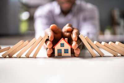 A man protecting a small model house from dominoes to represent holiday home insurance