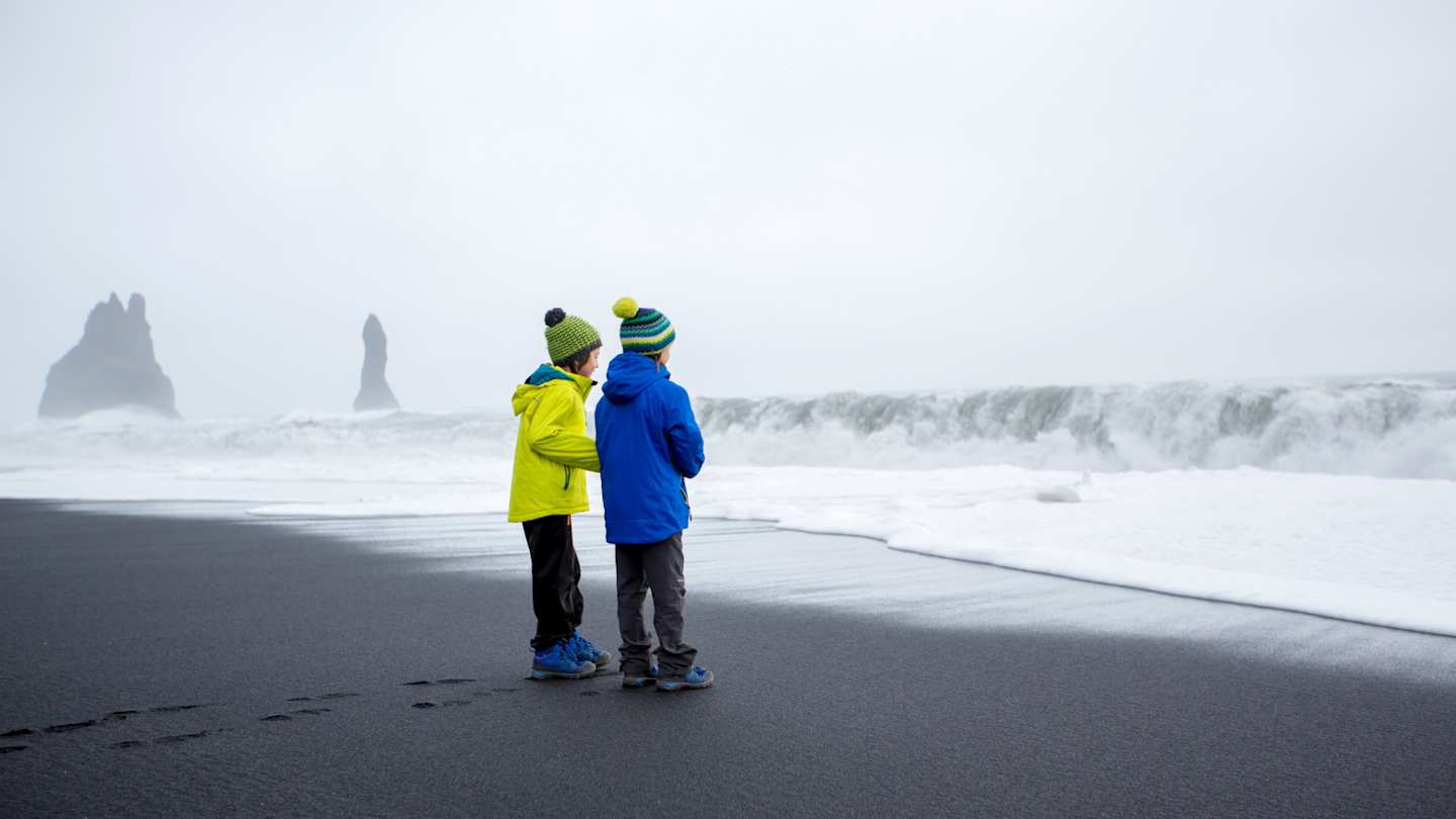 Two young children on the black sand beach of Reynisfjara on a misty day, Iceland