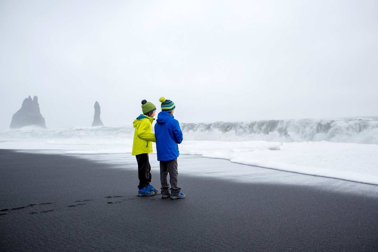 Two young children on the black sand beach of Reynisfjara on a misty day, Iceland