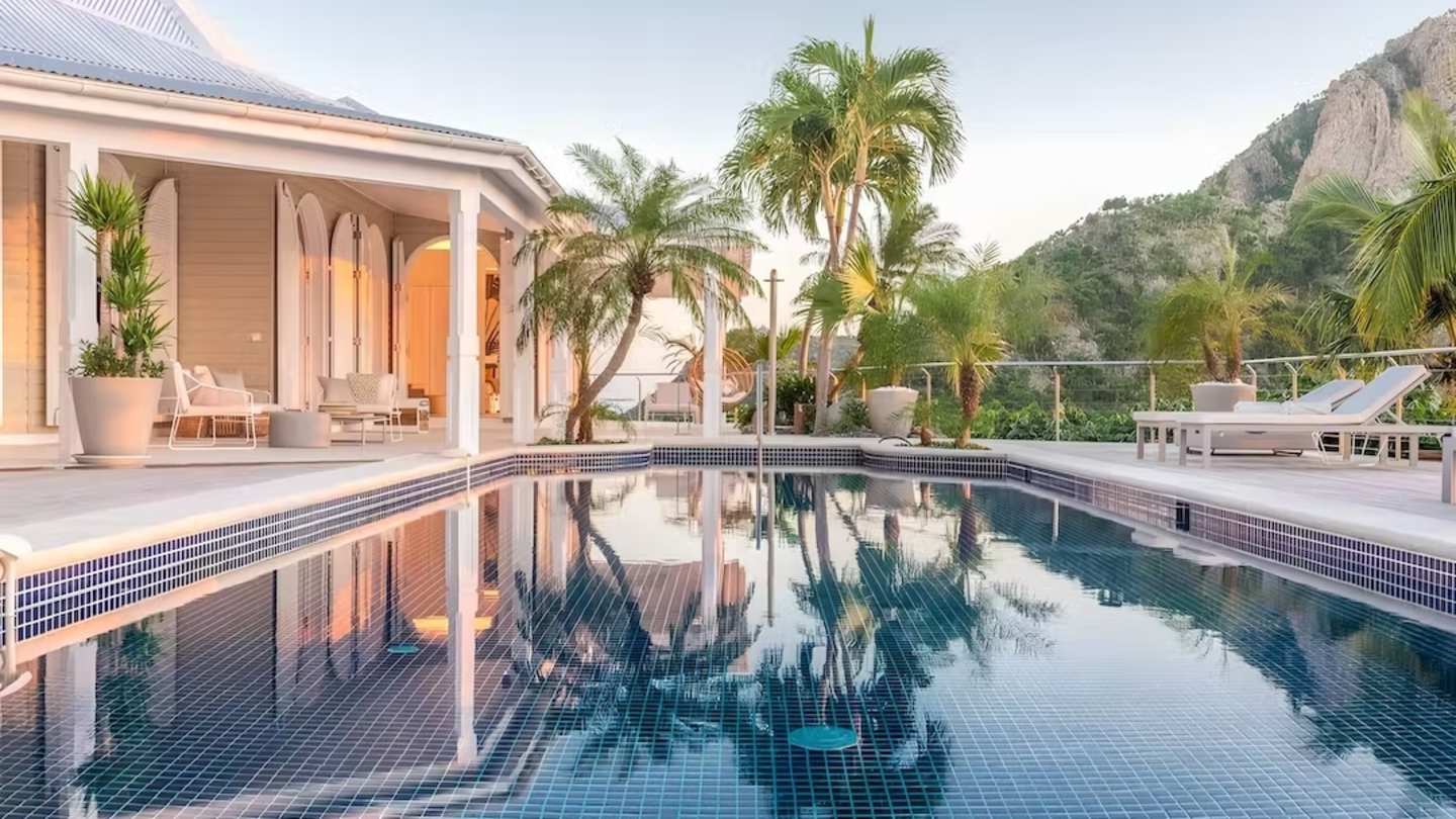 Palm trees reflecting in a pool with mountains in the background, The Colour of Love, Plum Guide home in Saint Barthélemy