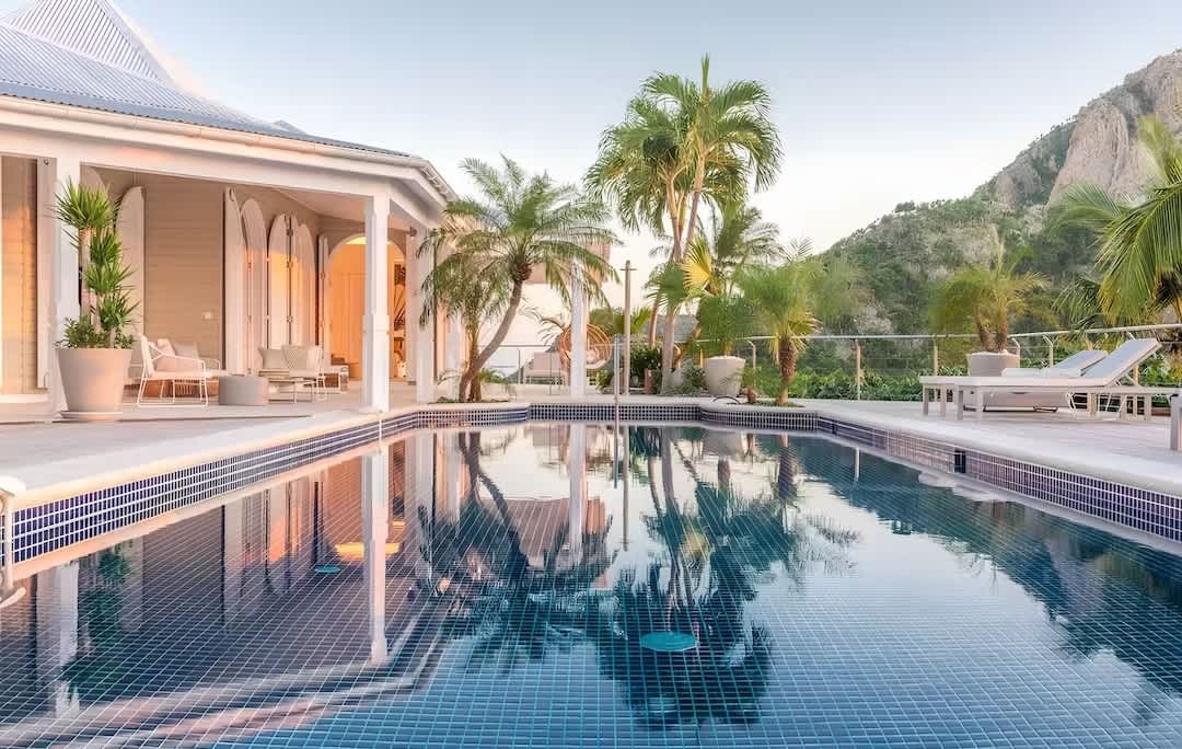 Palm trees reflecting in a pool with mountains in the background, The Colour of Love, Plum Guide home in Saint Barthélemy