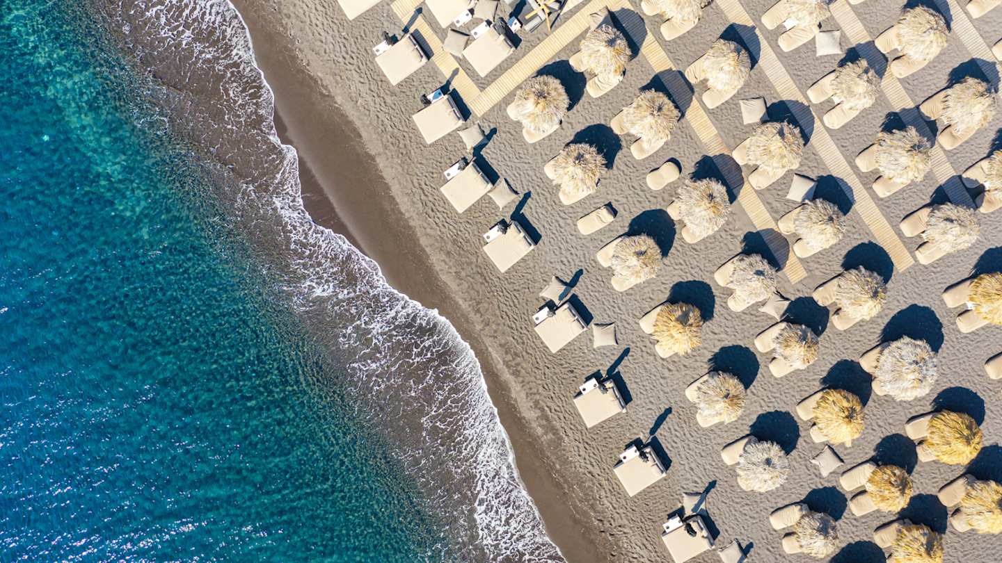 A bird's eye view of umbrellas and sun beds by the sea at Perissa Beach, Santorini, Greece