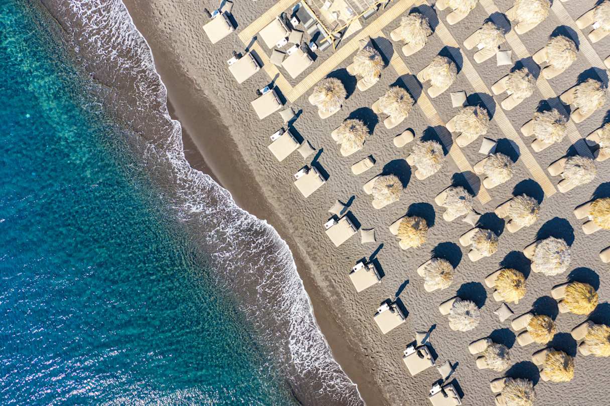 A bird's eye view of umbrellas and sun beds by the sea at Perissa Beach, Santorini, Greece