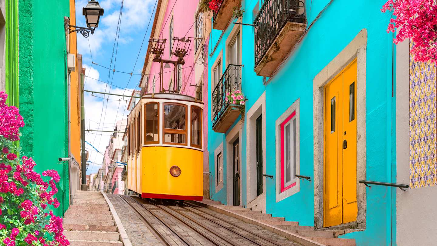 Yellow tram on a street with colourful houses and flowers on the balconies, going down the hill of Chiado in Lisbon, Portugal
