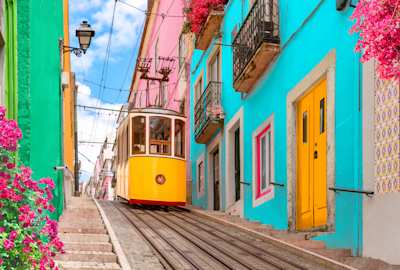 Yellow tram on a street with colourful houses and flowers on the balconies, going down the hill of Chiado in Lisbon, Portugal
