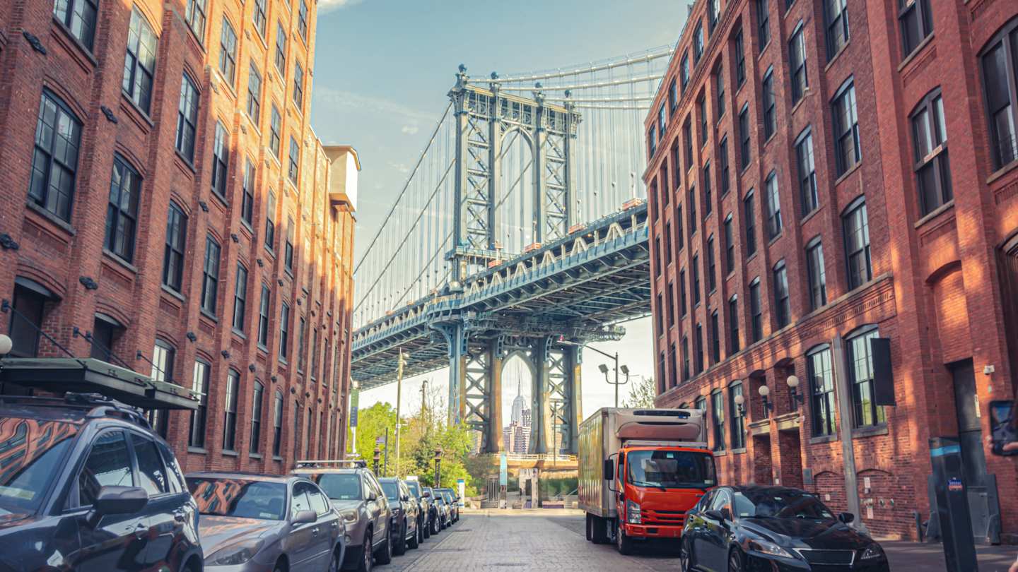 Manhattan Bridge seen from a narrow alley enclosed by two brick buildings on a sunny day in Brooklyn, New York City