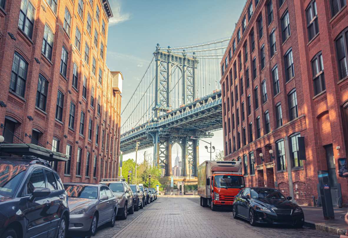 Manhattan Bridge seen from a narrow alley enclosed by two brick buildings on a sunny day in Brooklyn, New York City