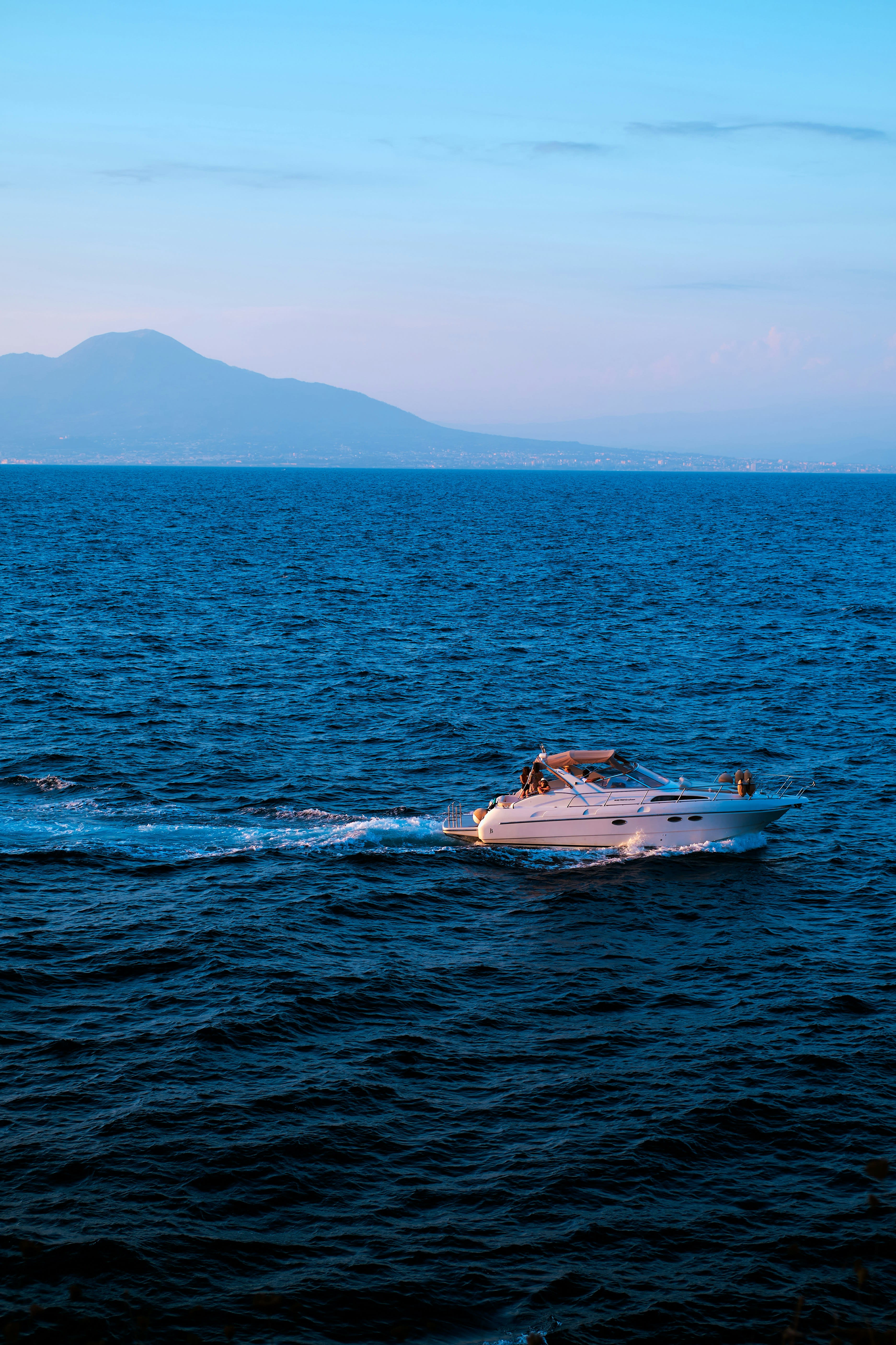 Private boat gliding along the sea in Sorrento on a summer's evening with pink skies and hills in the distance.
