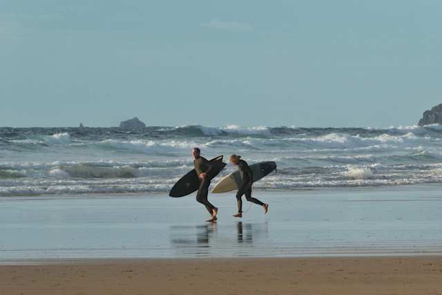 People with surfboards running towards the sea at Watergate Beach, Newquay, Cornwall, England, UK