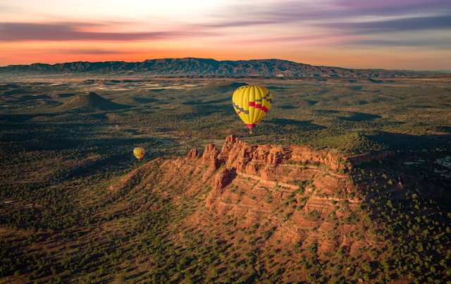 An aerial view of a hot air balloon over a large plain and tall brown cliff, Sedona, Arizona, USA