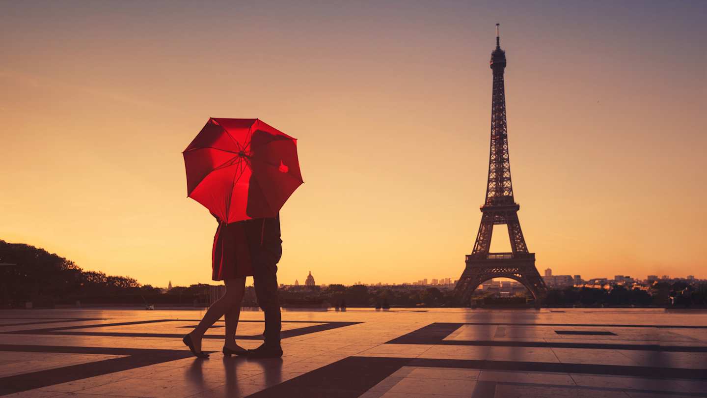 A couple standing behind a red umbrella admiring the Eiffel Tower, Paris, France
