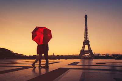 A couple standing behind a red umbrella admiring the Eiffel Tower, Paris, France