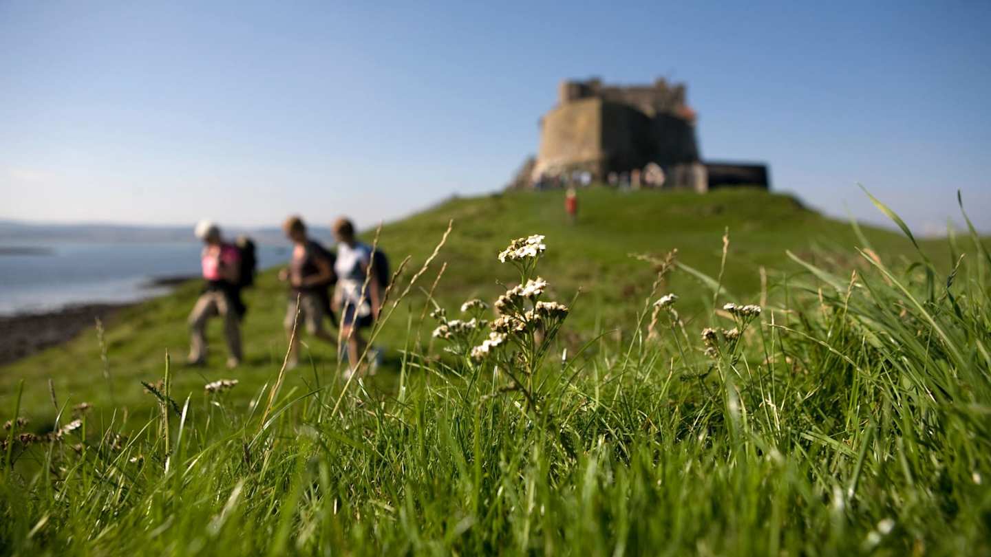 People walking on a hill by a castle on a sunny day in Northumberland, England, UK