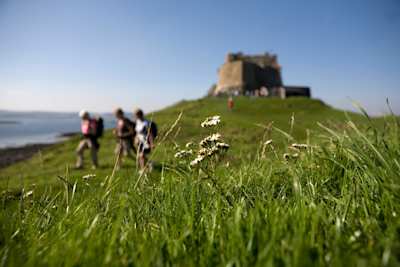 People walking on a hill by a castle on a sunny day in Northumberland, England, UK