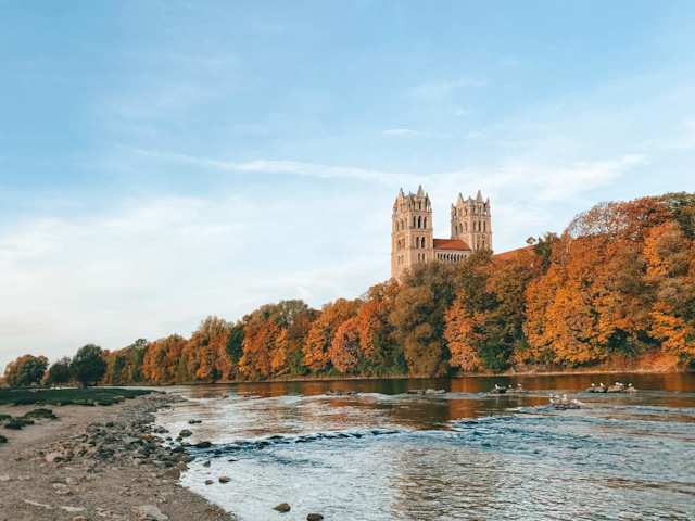 A castle standing tall above orange and brown trees behind a river in Munich, Germany