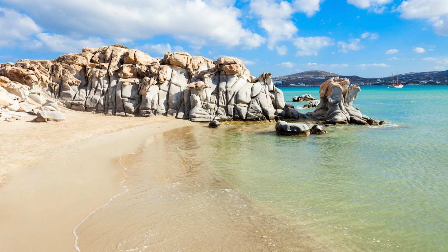 Waves gently rolling onto the sand in front of large grey rocks at Kolymbithres Beach, Paros, Greece