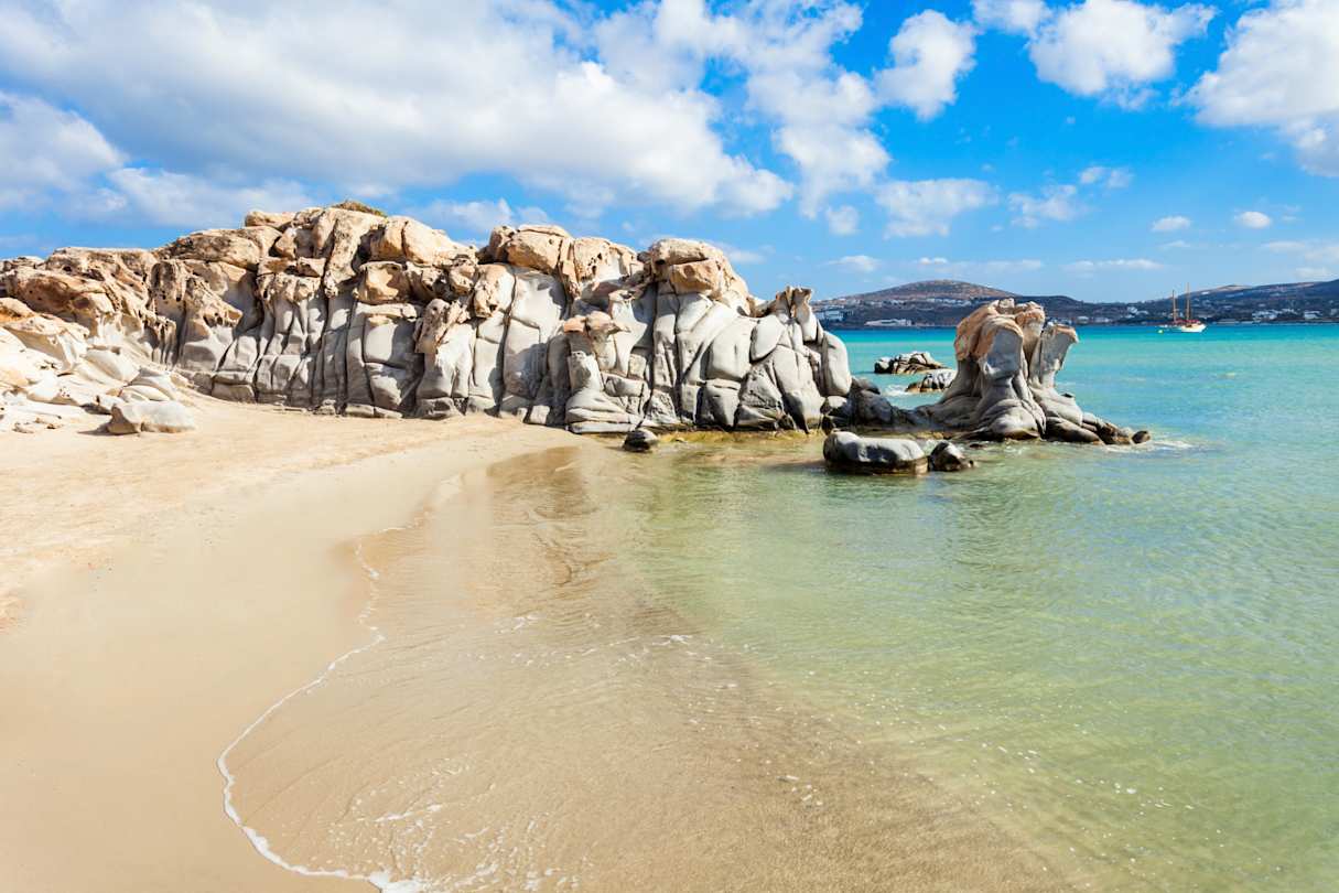 Waves gently rolling onto the sand in front of large grey rocks at Kolymbithres Beach, Paros, Greece