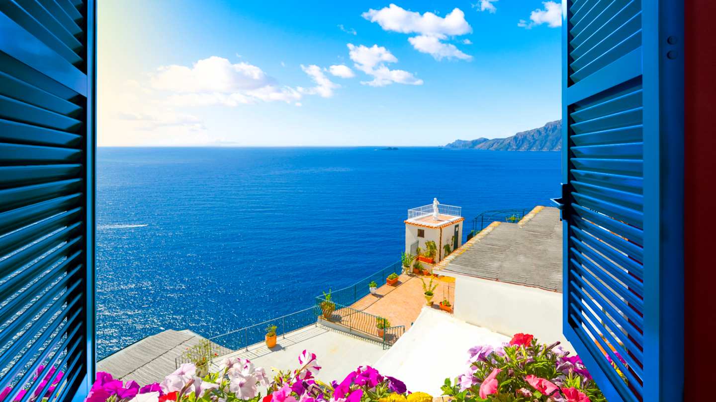 Scenic view from an open window with blue shutters and pink flowers of the Mediterranean Sea, Amalfi Coast