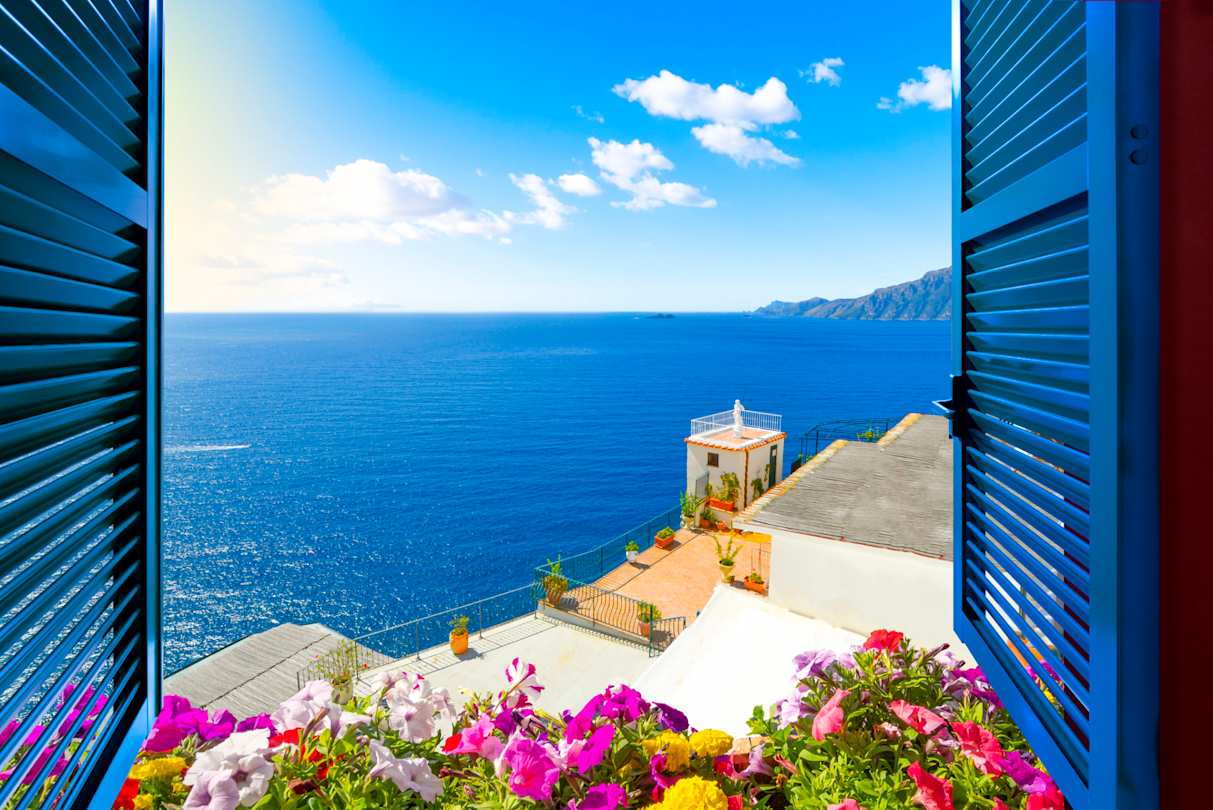 Scenic view from an open window with blue shutters and pink flowers of the Mediterranean Sea, Amalfi Coast