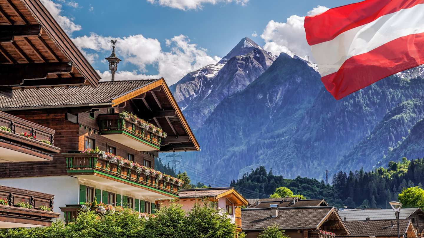 A large wooden lodge in front of the Kitzsteinhorn glacier and an Austrian flag in Salzburg, Austrian Alps, Austria