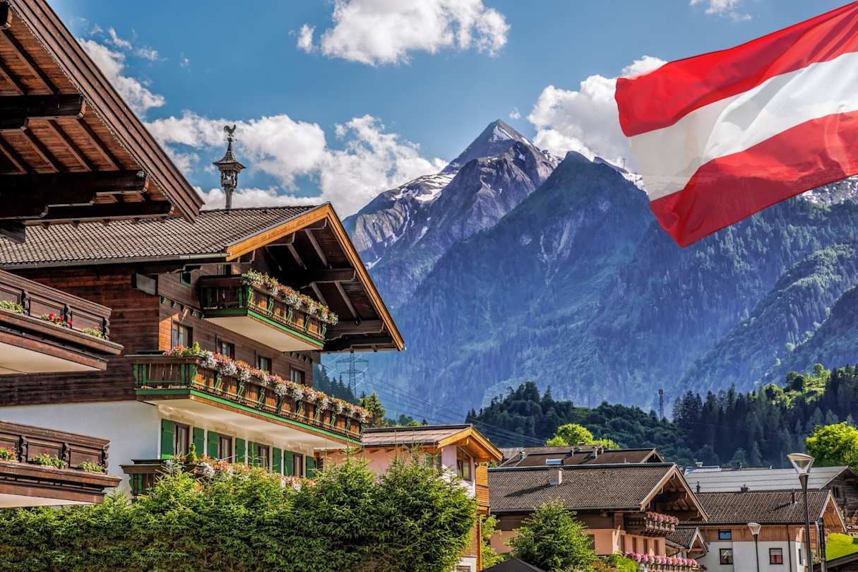 A large wooden lodge in front of the Kitzsteinhorn glacier and an Austrian flag in Salzburg, Austrian Alps, Austria