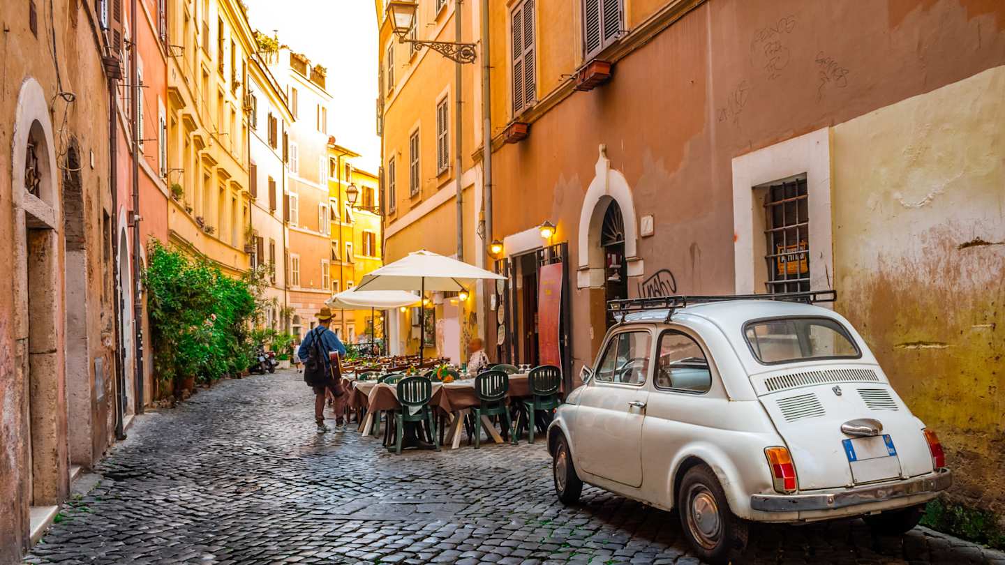 Charming cobbled street in Trastevere with sidewalk cafe and vintage Fiat 500, Rome, Italy