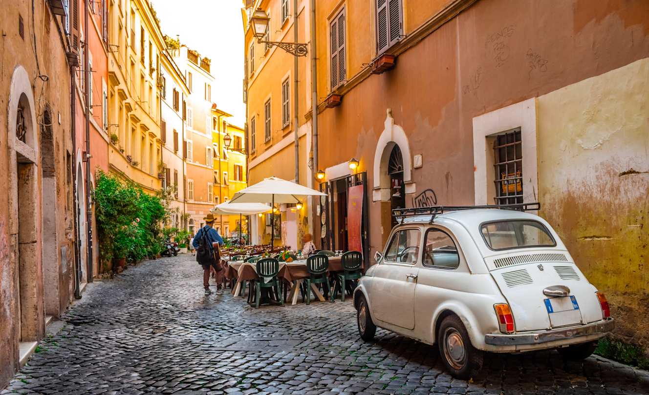 Charming cobbled street in Trastevere with sidewalk cafe and vintage Fiat 500, Rome, Italy