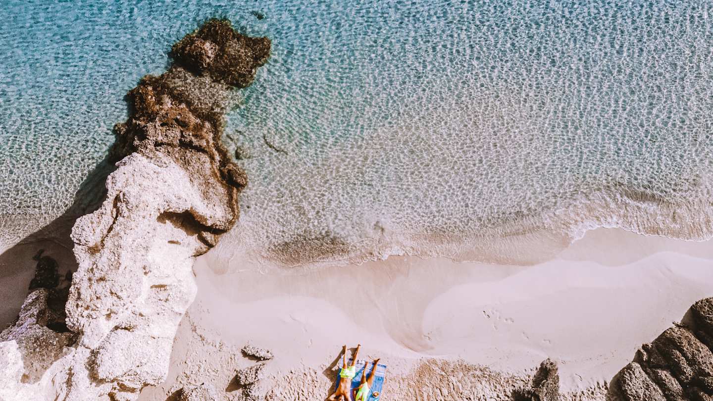 A bird's eye view of a couple sunbathing together on a pristine beach in Crete, Greece