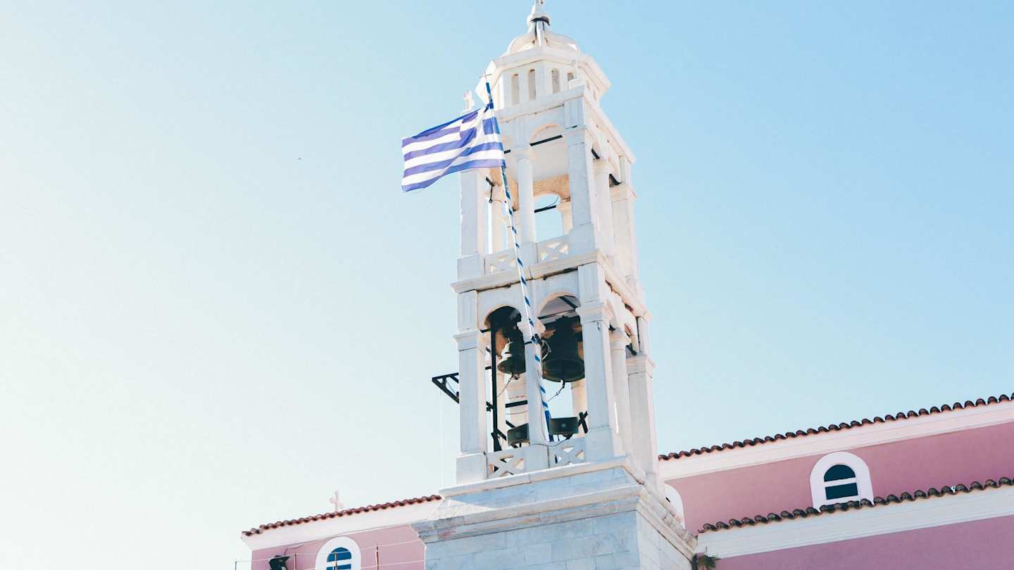 A close up of a church tower with bells and a Greek flag in Skiathos, Greece