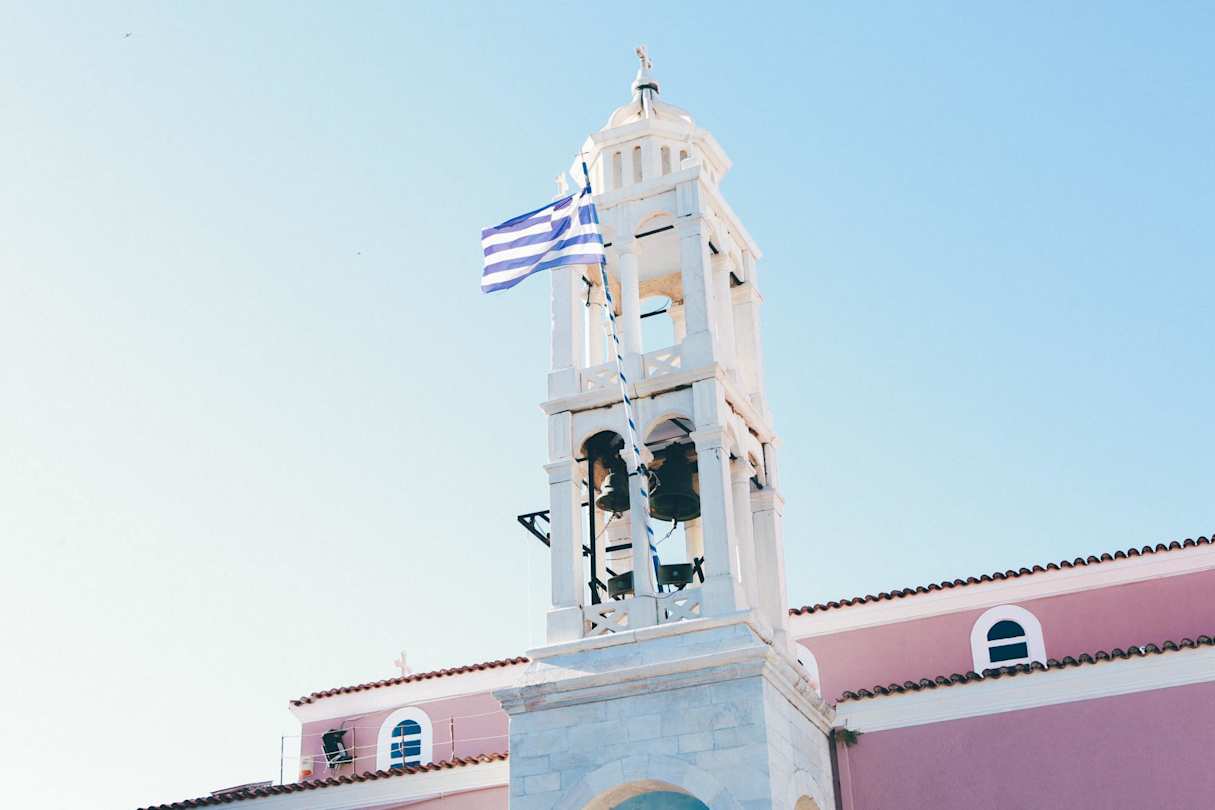A close up of a church tower with bells and a Greek flag in Skiathos, Greece