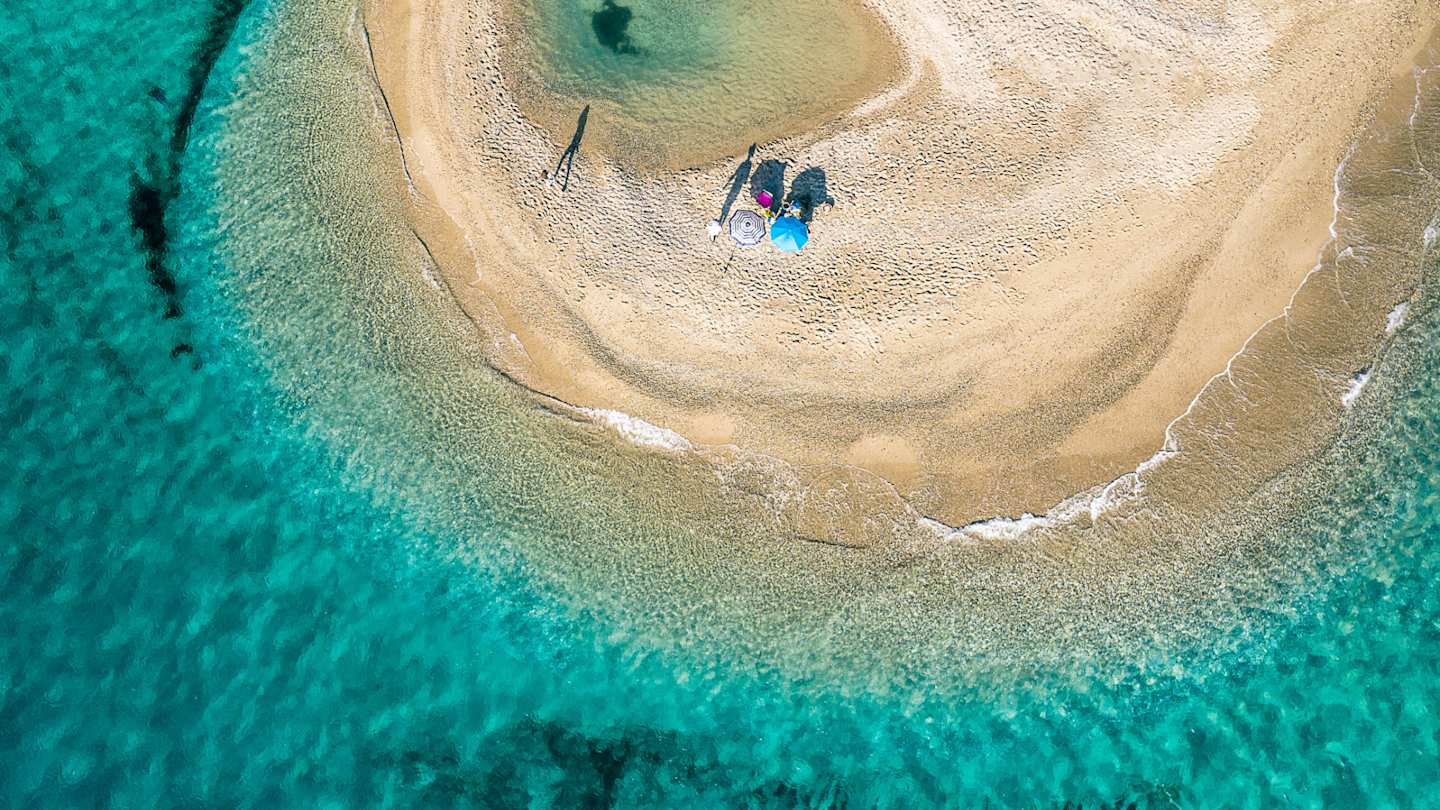 A bird's eye view of two umbrellas on the golden sand by clear turquoise water at Possidi Beach, Halkidiki, Greece