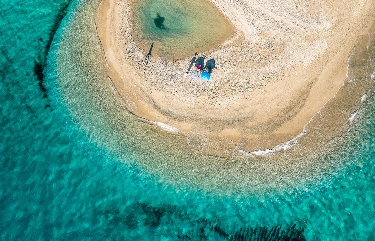 A bird's eye view of two umbrellas on the golden sand by clear turquoise water at Possidi Beach, Halkidiki, Greece