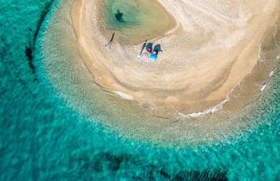 A bird's eye view of two umbrellas on the golden sand by clear turquoise water at Possidi Beach, Halkidiki, Greece