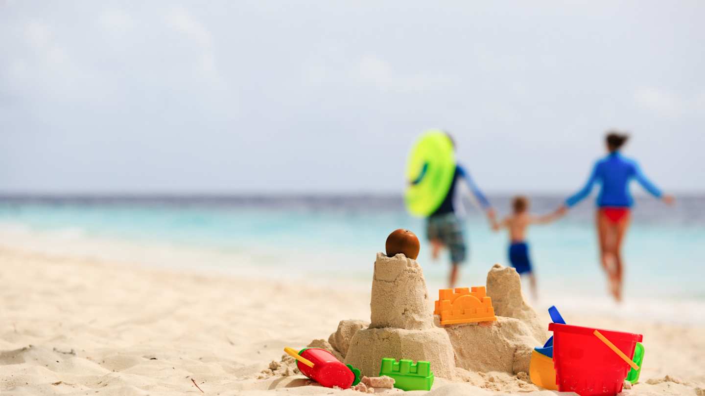A close up view of a sandcastle and some beach toys in front of a young family in the background at the beach
